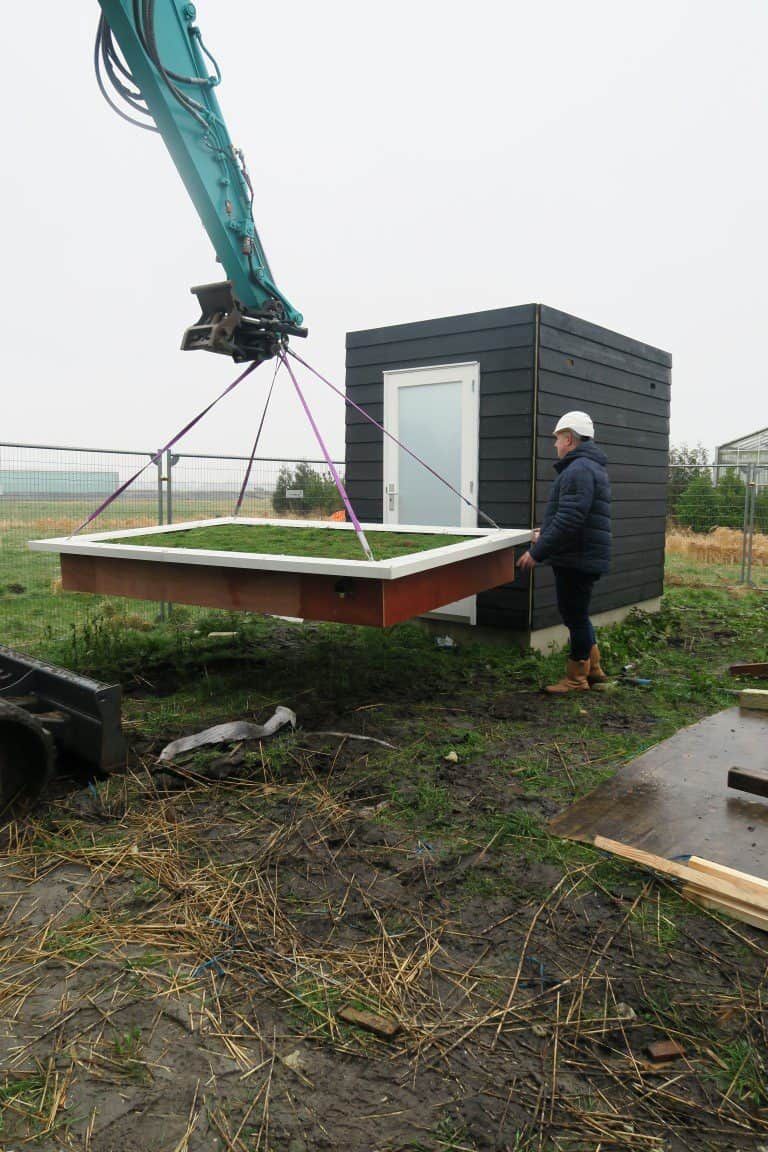 Zwart houten schuurtje in een grasveld met opgetild dak