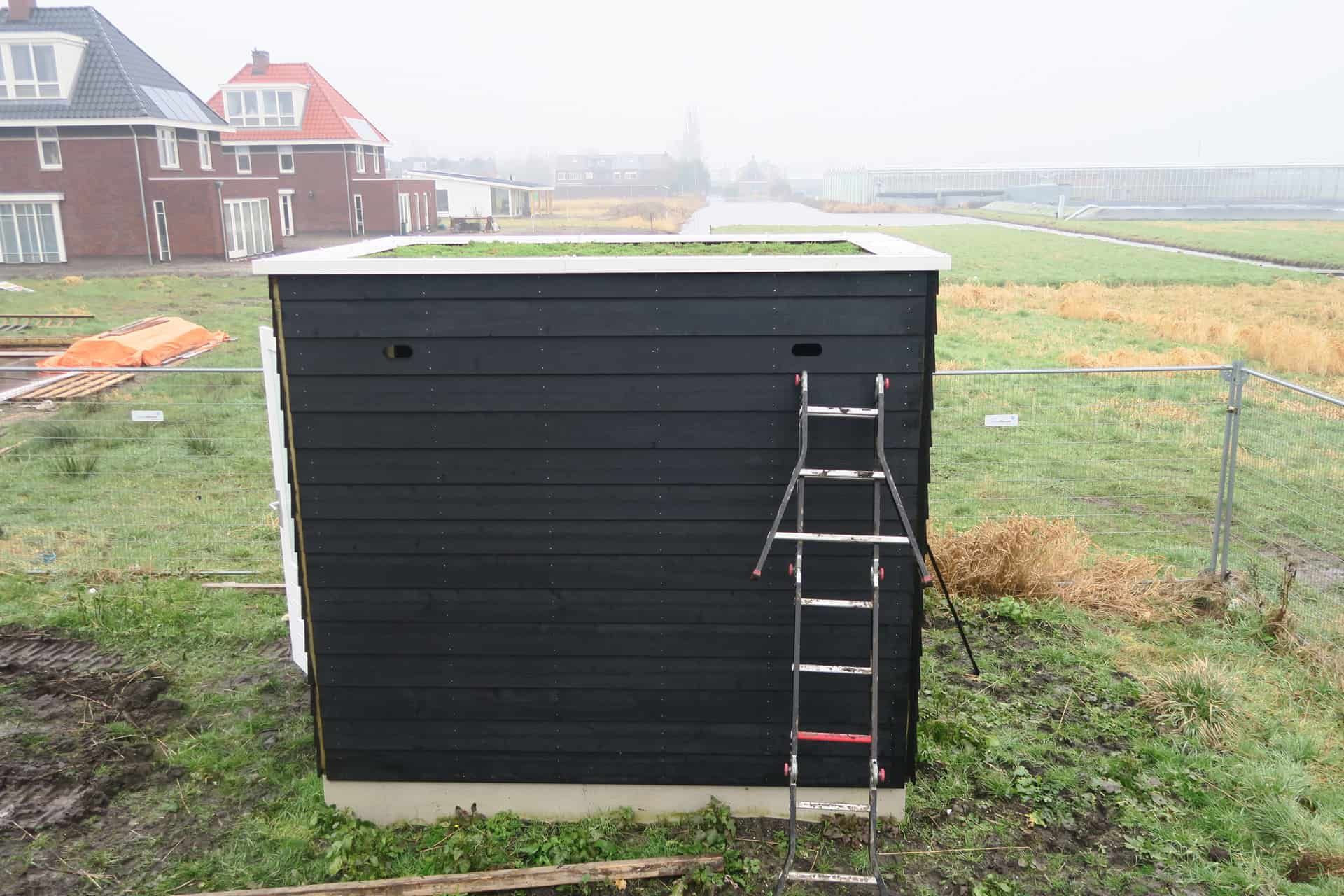 Zwart houten schuurtje in een grasveld met ladder