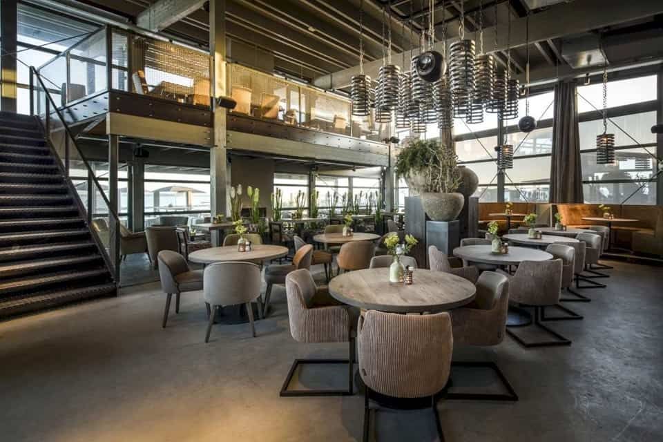 Industrieel restaurant van binnen met met ronde tafels en grijze stoelen
