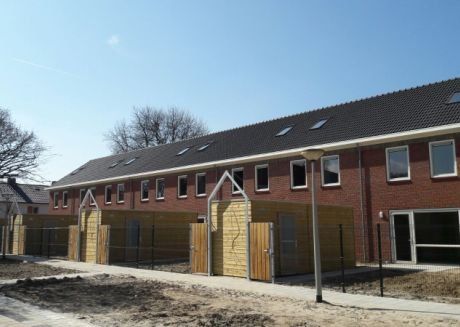 Nieuwbouwhuizen met rode stenen en zwart dak met gele schuttingen met zand in voortuin