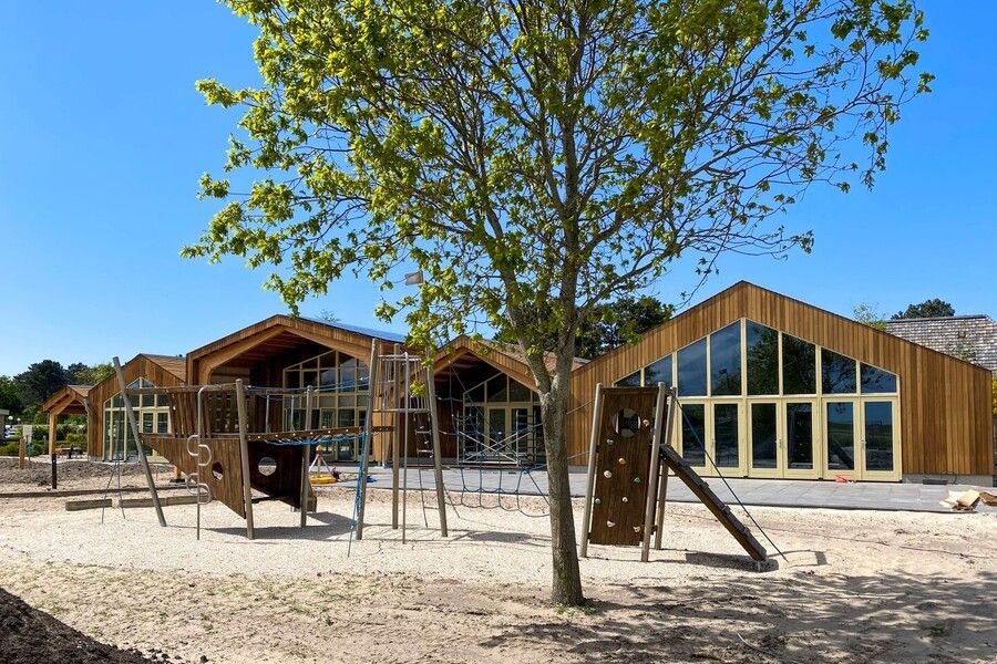 Houten gebouwen van veraf met speeltoestellen en een boom