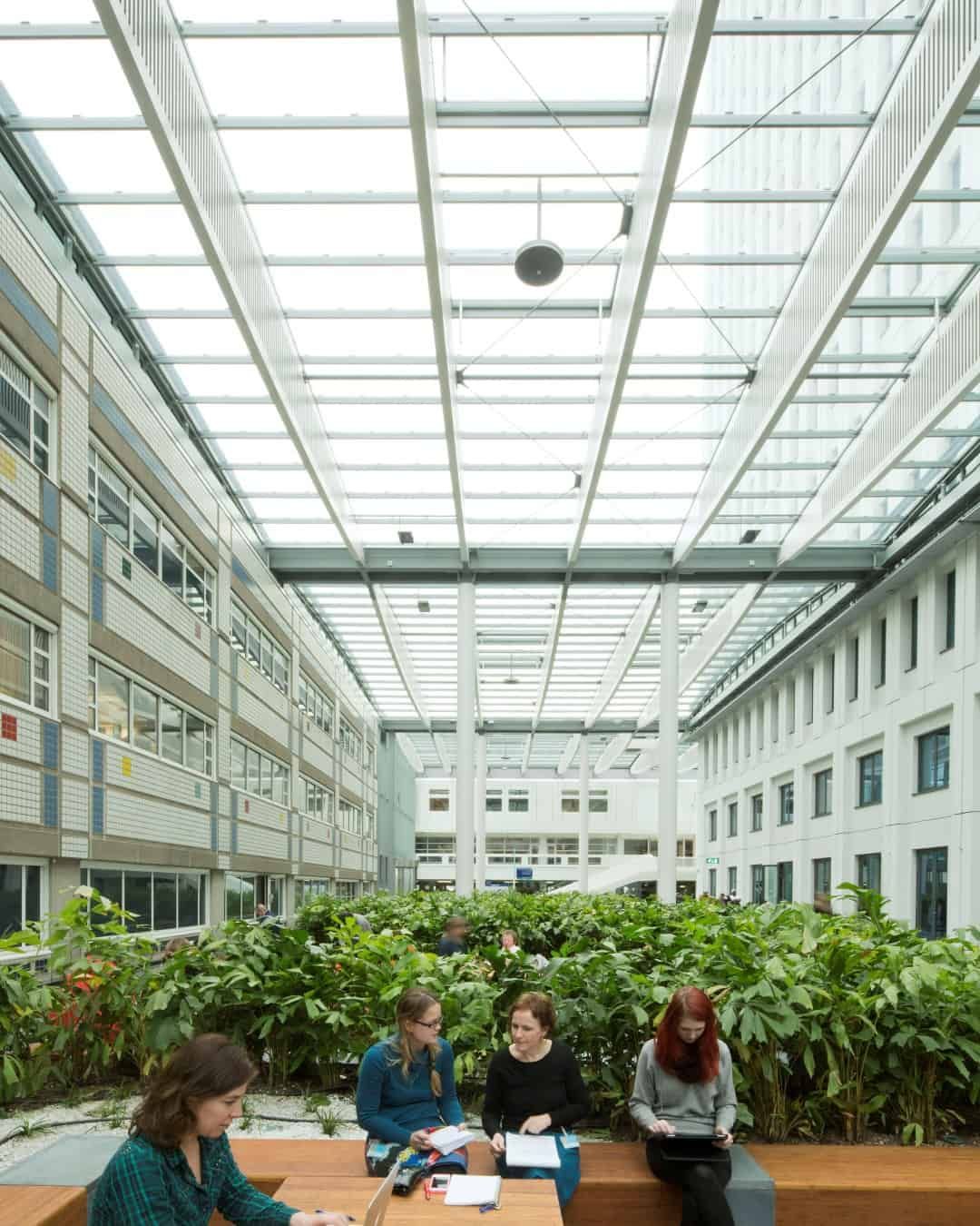 Wit gebouw van binnen met glazen dak, groene planten en mensen