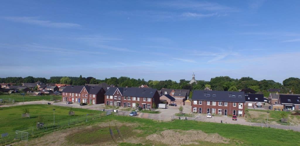 Vooraanzicht van nieuwbouw wijk met blauwe lucht en groen gras op de voorgrond
