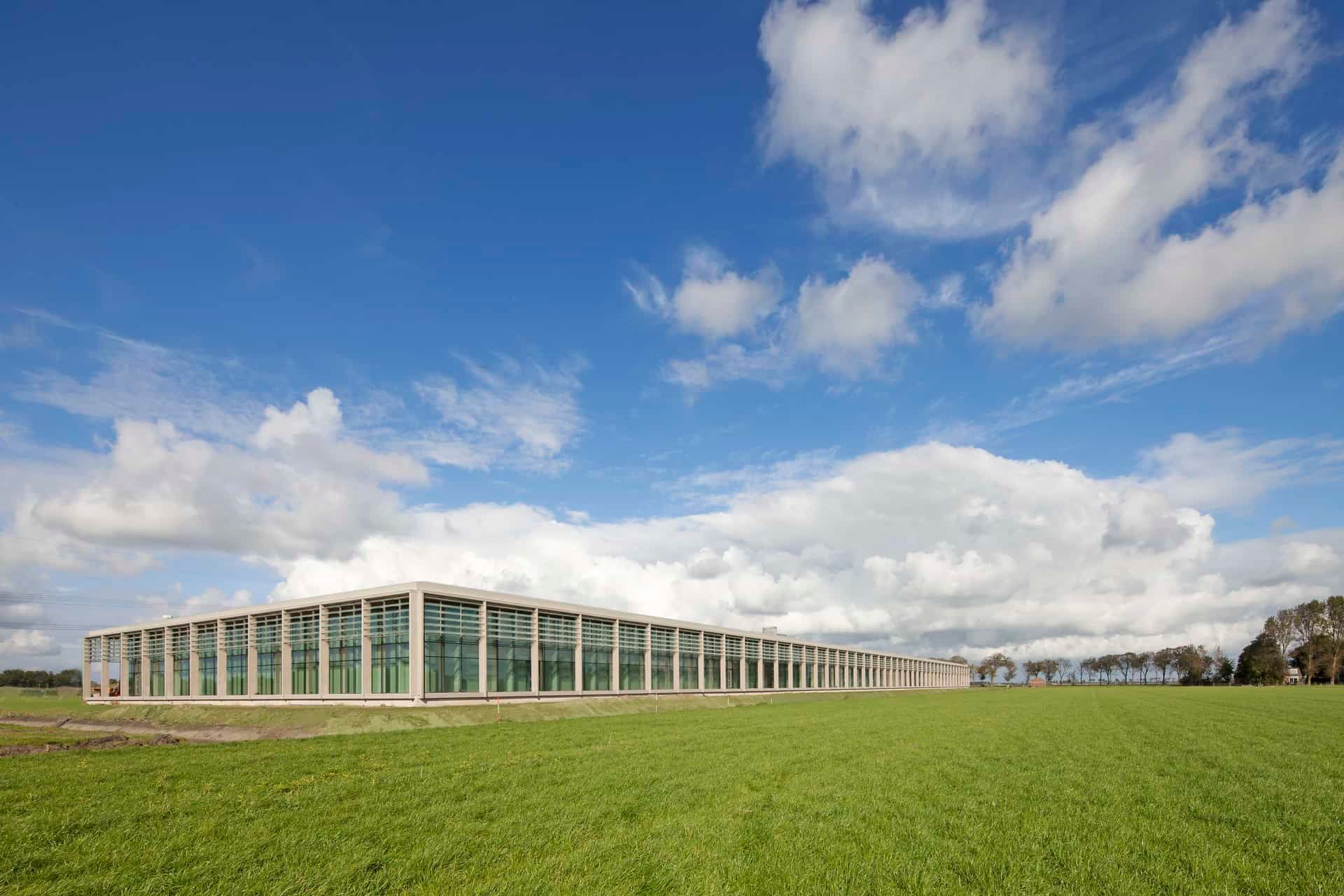 Houten gebouw met veel ramen van veraf met een grasveld ervoor