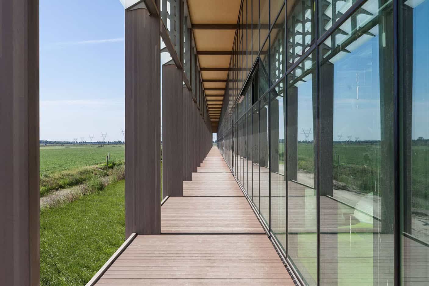 De buitenkant van een gebouw met veel glas en houten pilaren met overdekt gedeelte en gras