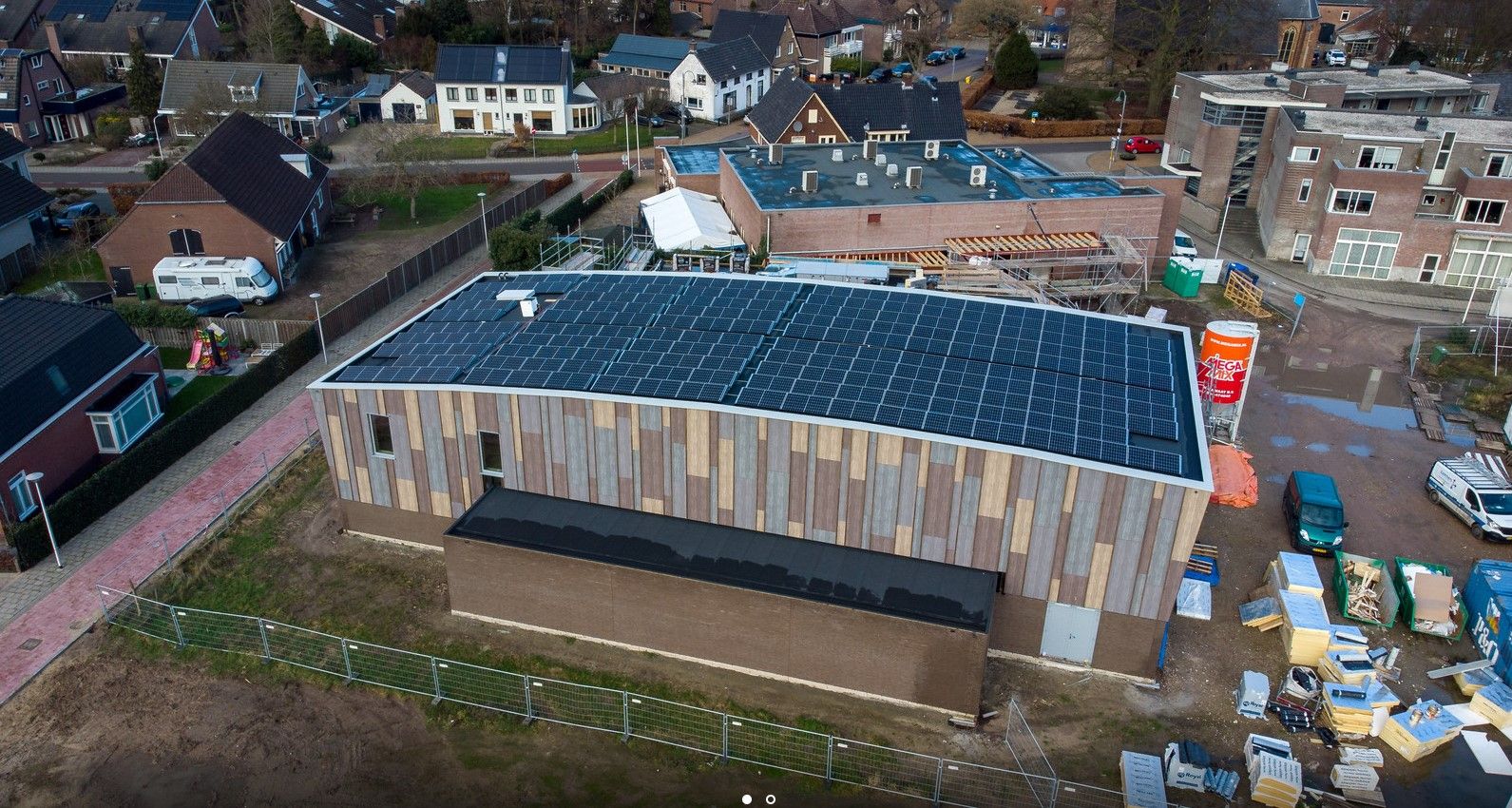 Gebouw met verschillende kleuren hout en zonnepanelen op het dak in een woonwijk