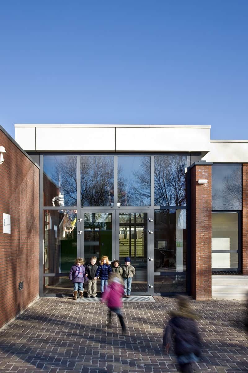 Glazen ingang van een gebouw van bakstenen met kinderen ervoor