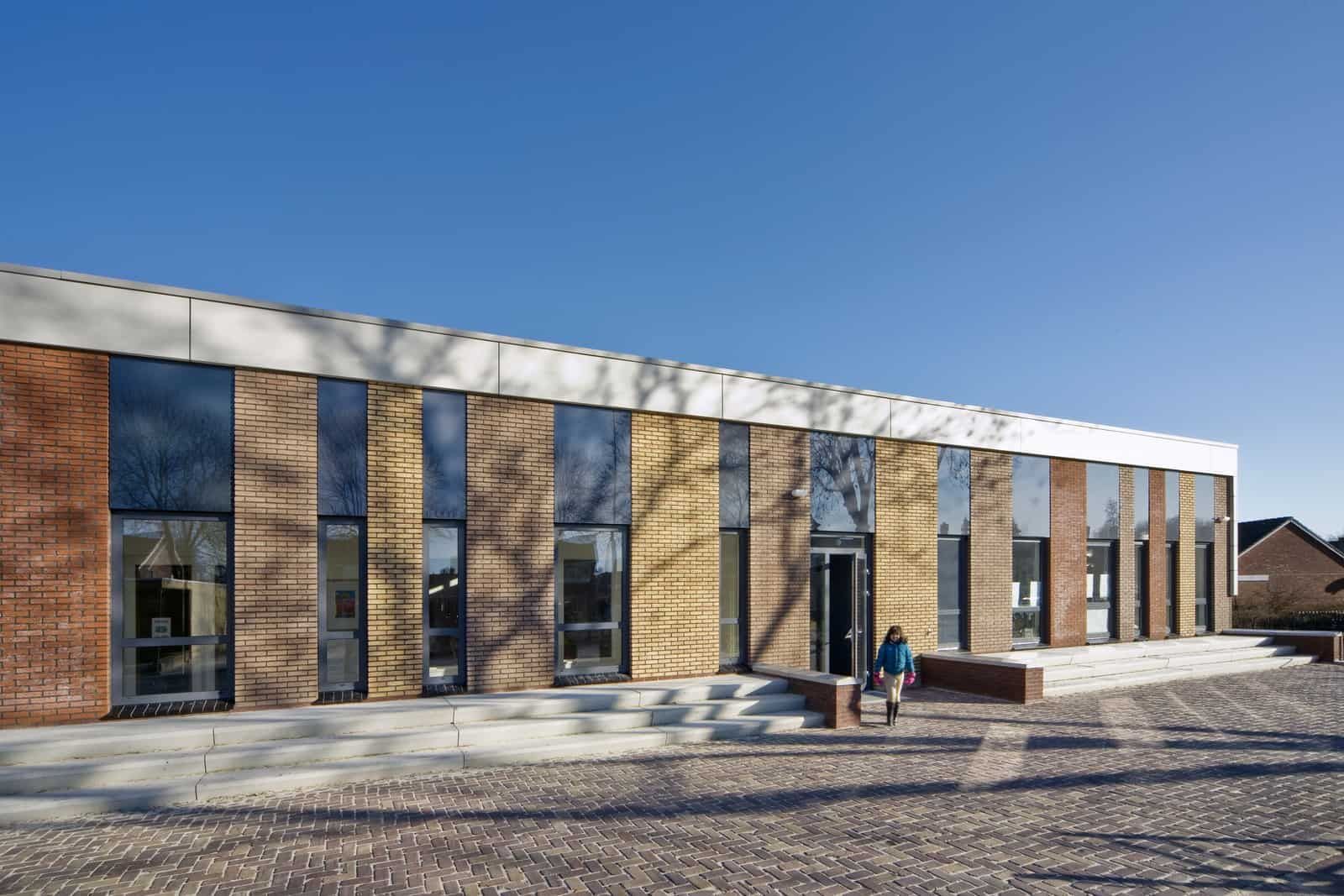 Gebouw met verschillende kleuren bakstenen en lange ramen met een trap ervoor