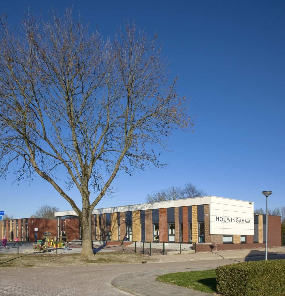 Gebouw van Houwingaham van veraf met een boom ervoor en speelplein