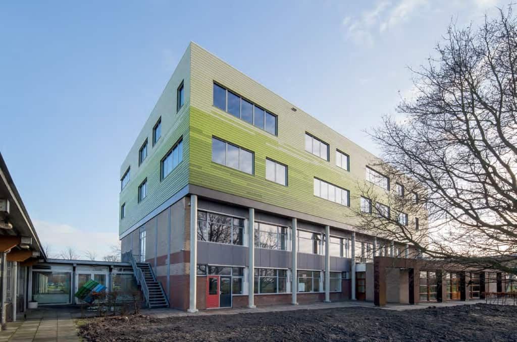 Gebouw met glazen onderkant en groene bovenkant met een boom ervoor