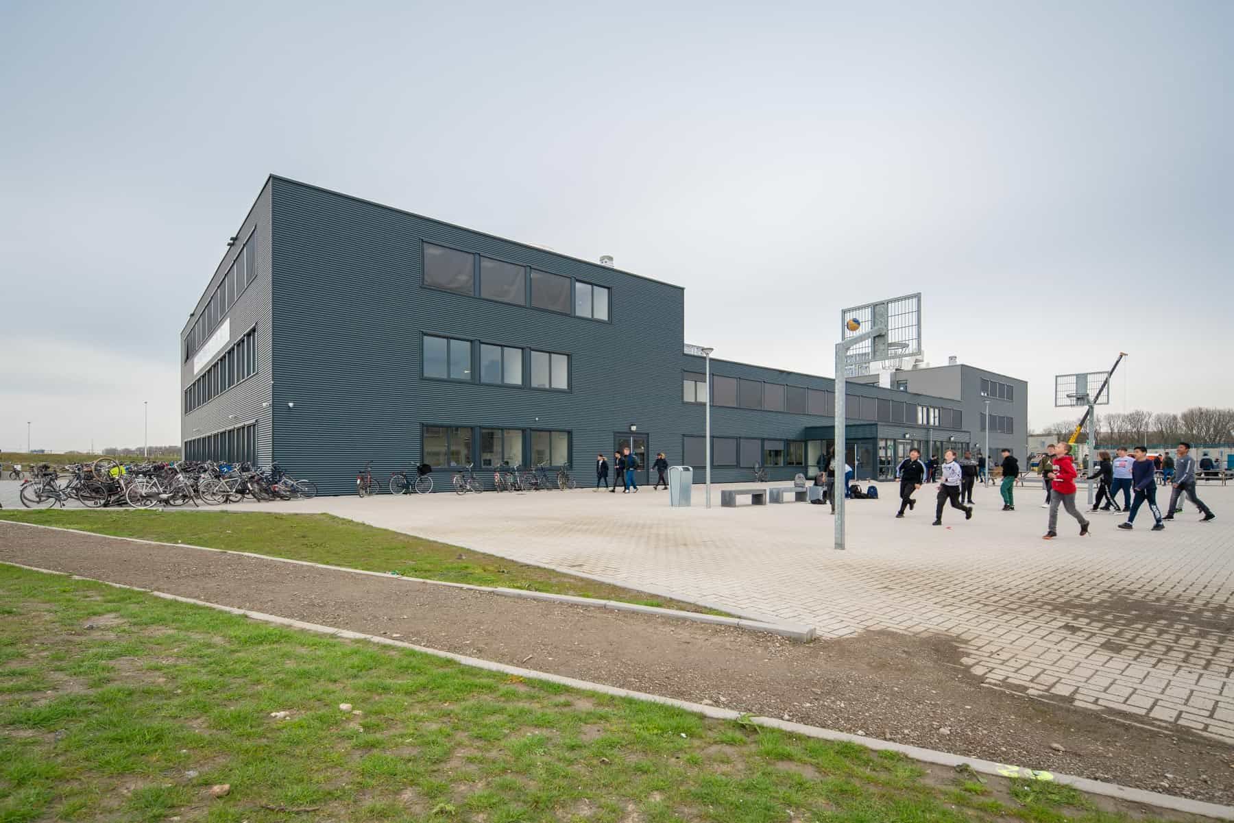 Het grijze gebouw van de Nuovo scholengroep met een grasveld en plein