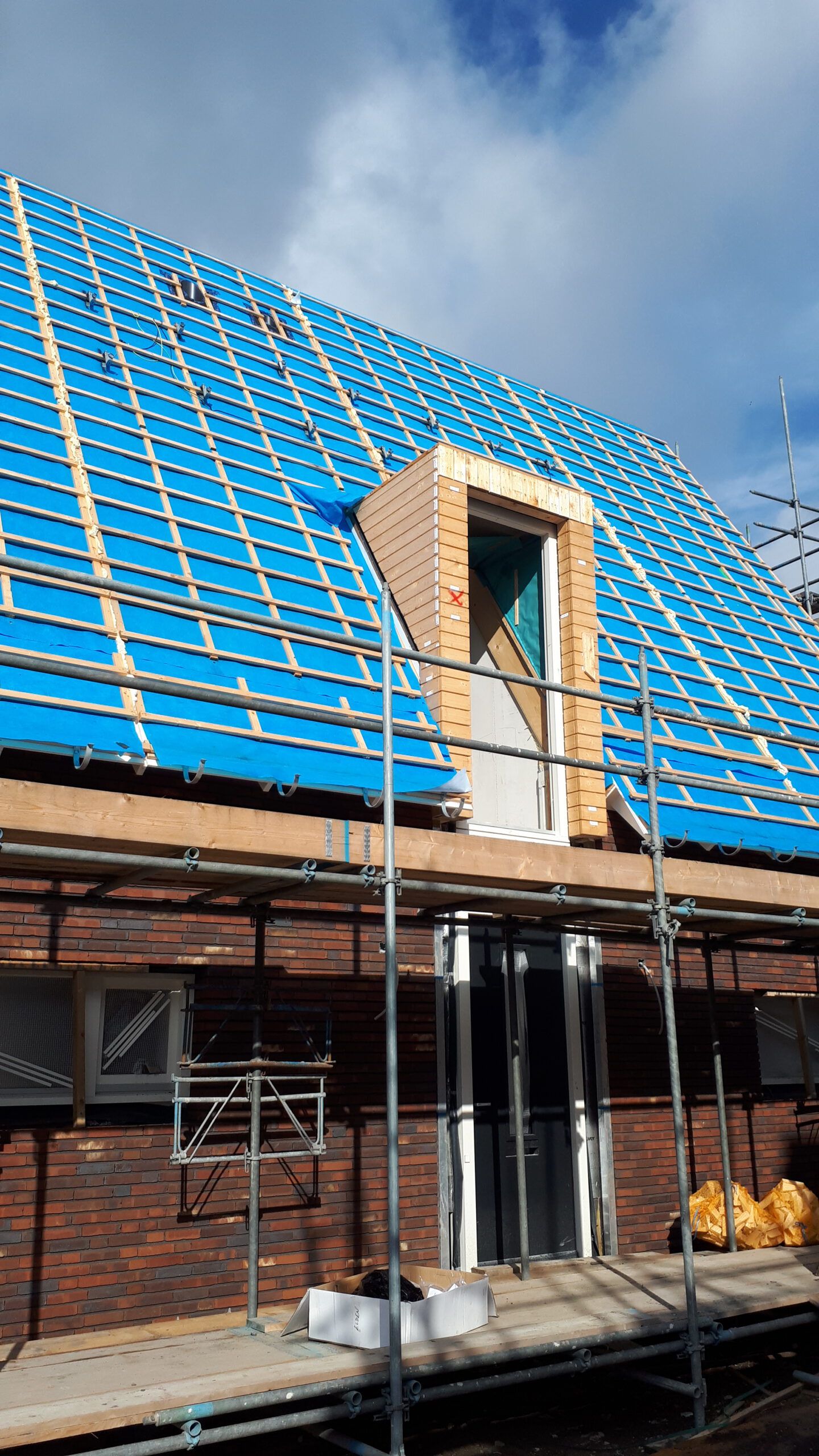 Huis in aanbouw met rode baksteden en een blauw dak met steigers eromheen