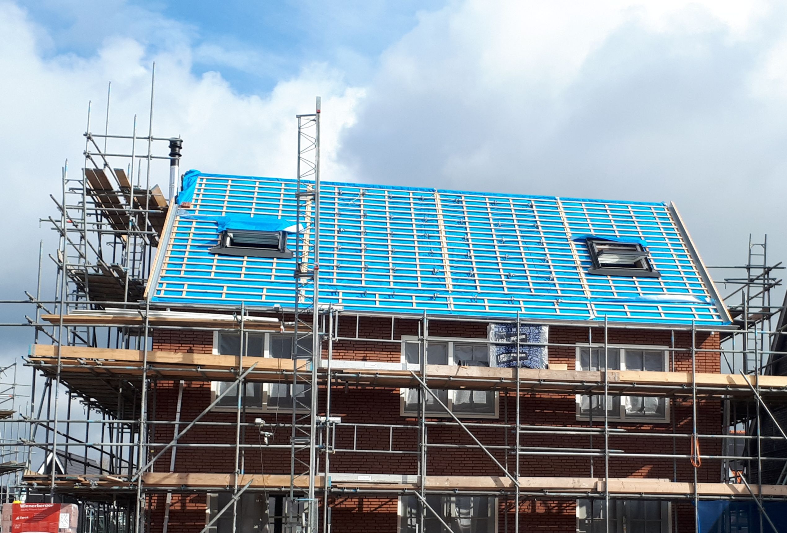Huis in aanbouw van rood baksteen met een blauw dak met steigers om het huis