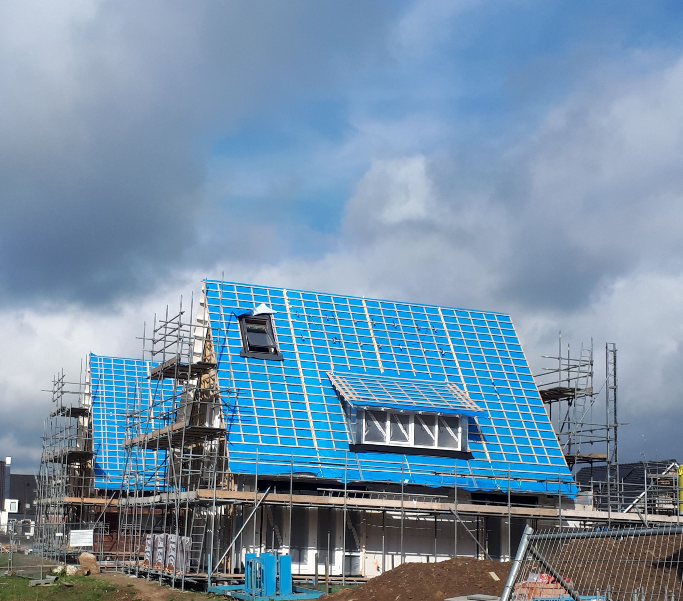 Huis in aanbouw met witte onderkant en blauw dak en steigers om het huis