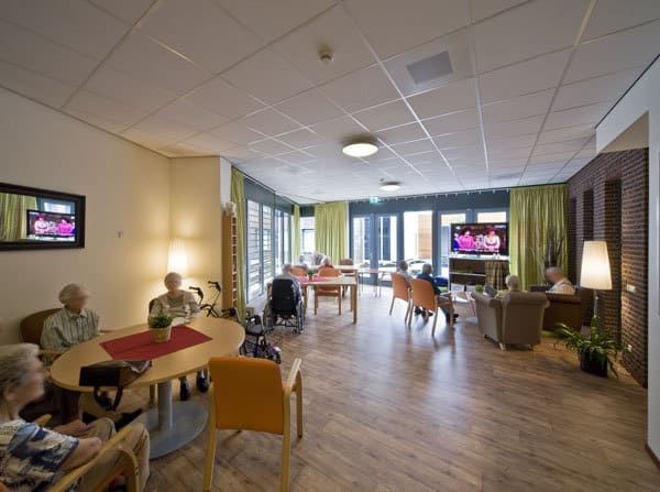 De gemeenschappelijke ruimte met de ouderen op stoelen en aan tafels