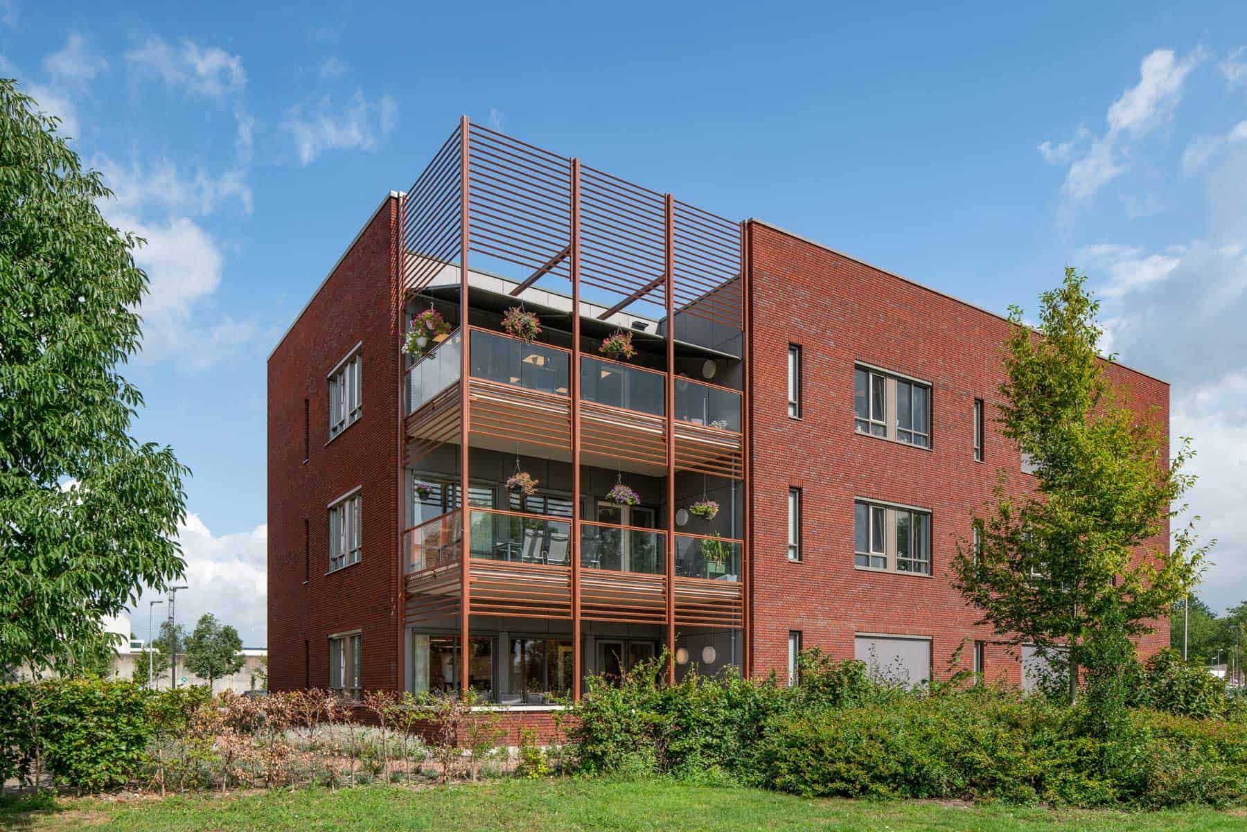 De hoek van het bakstenen gebouw met balkons met glas en planten