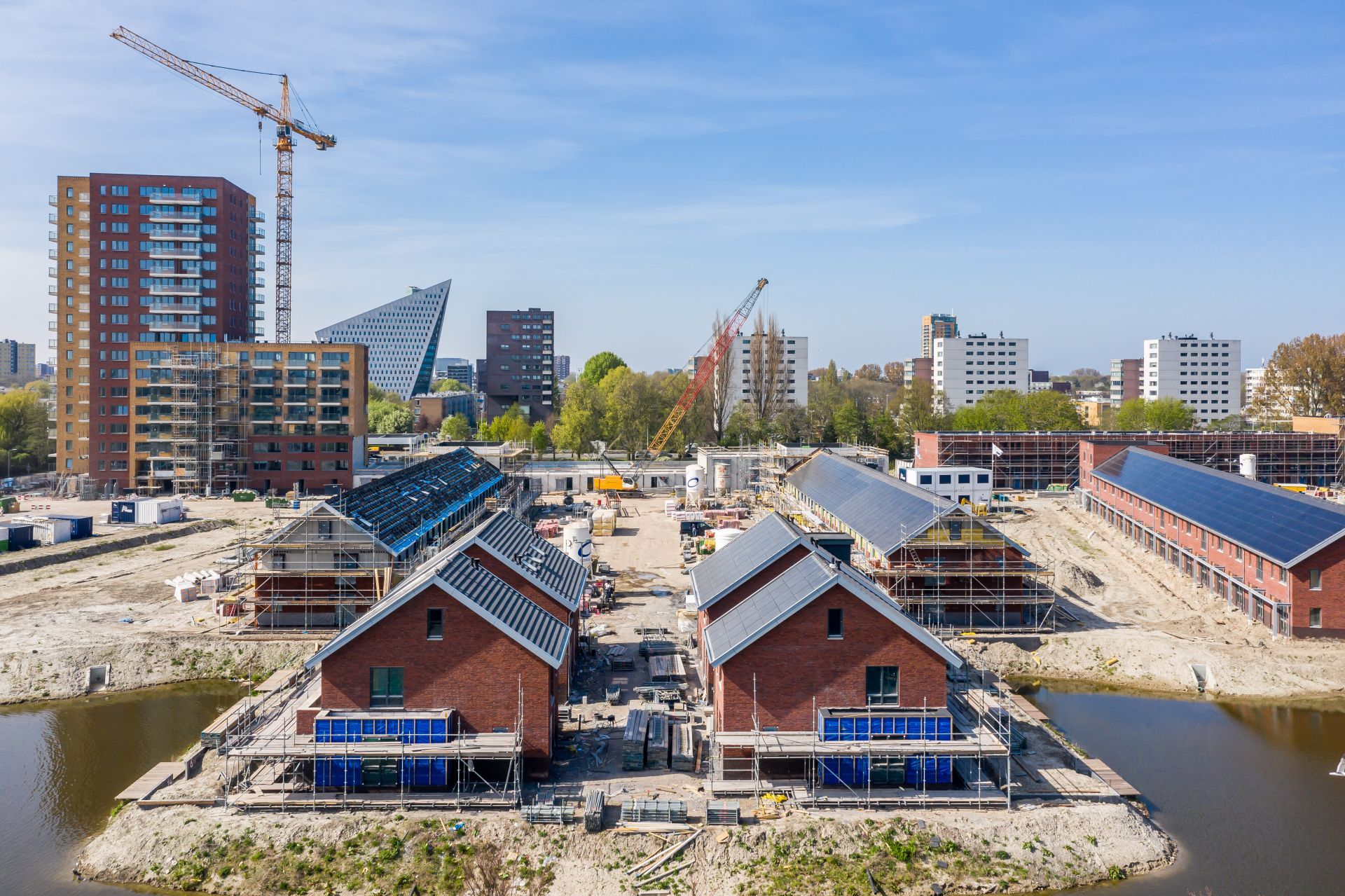 Zijkant van woonwijk in aanbouw met veel zand, water en hoge gebouwen erachter