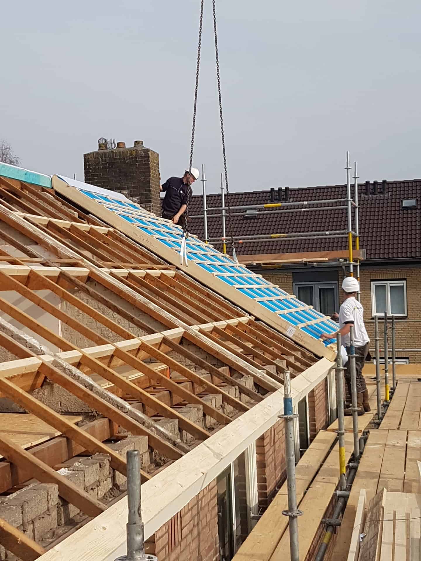 Houten dak in aanbouw met blauwe plaat en twee mensen aan het werk