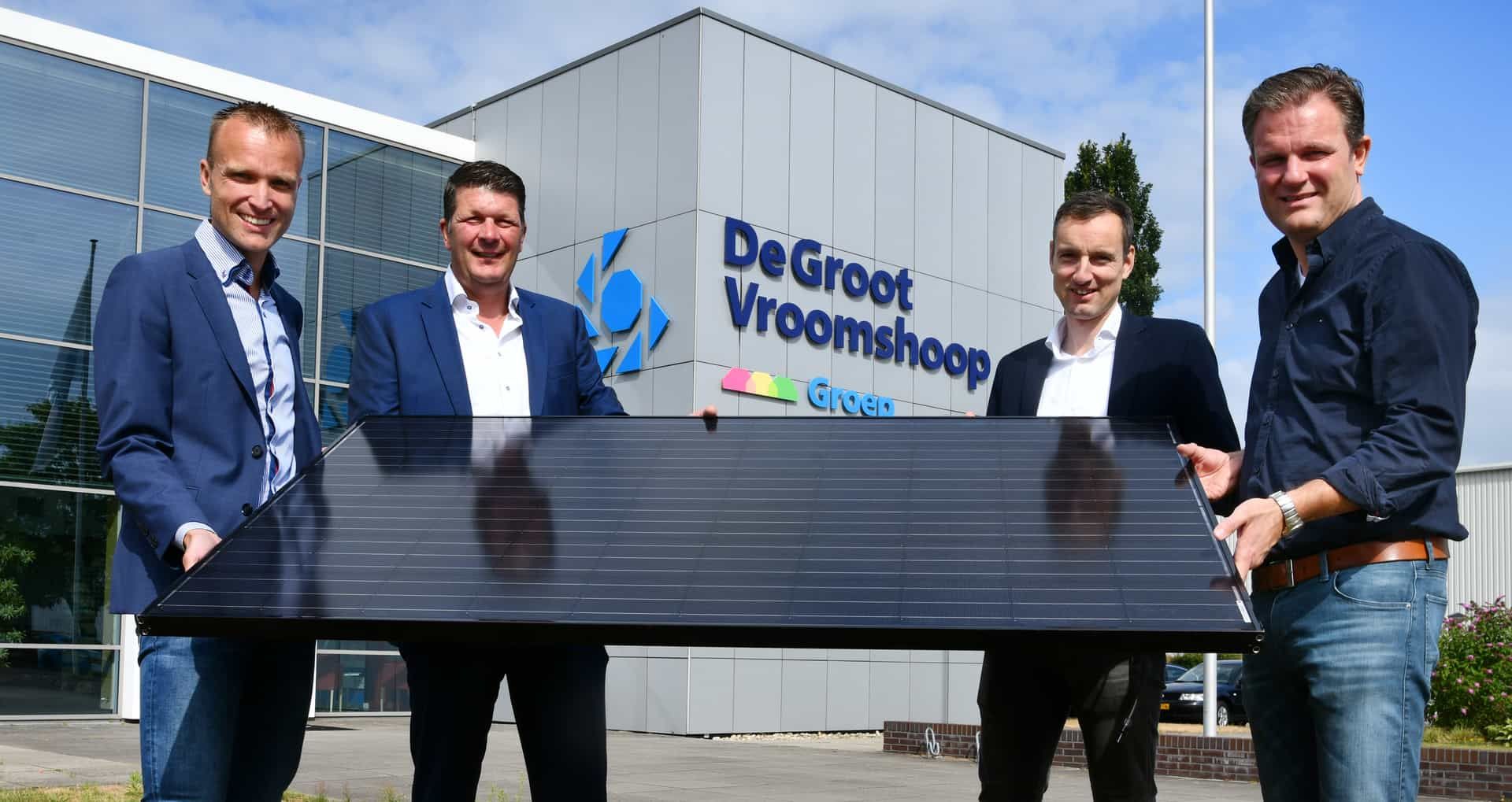 Vier mannen die een zonnepaneel vasthouden voor het gebouw van De Groot Vroomshoop