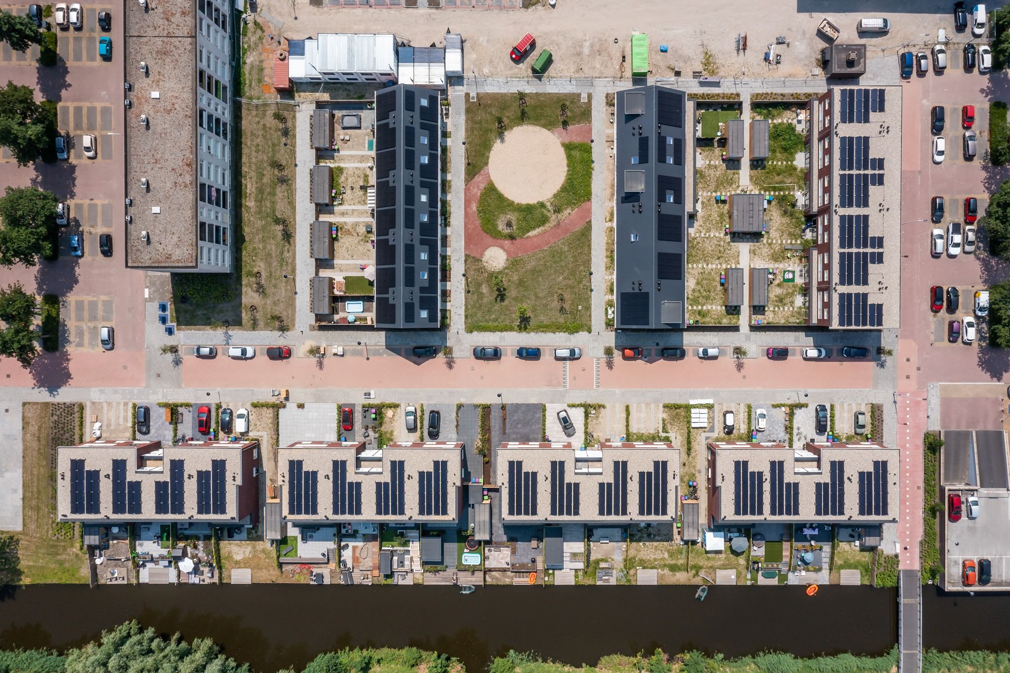 Een woonwijk met veel huizen, groen, parkeerplaatsen, aan het water van bovenaf