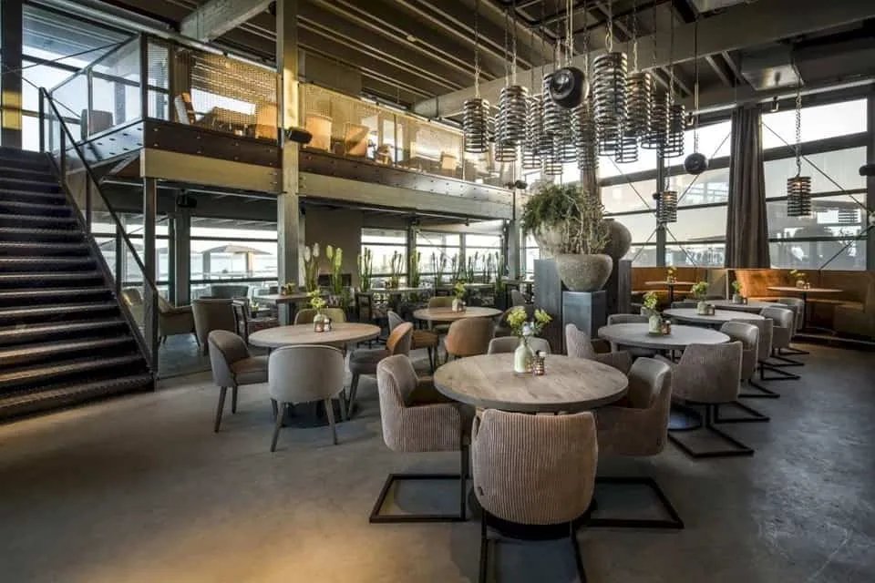 Industrieel restaurant van binnen met met ronde tafels en grijze stoelen