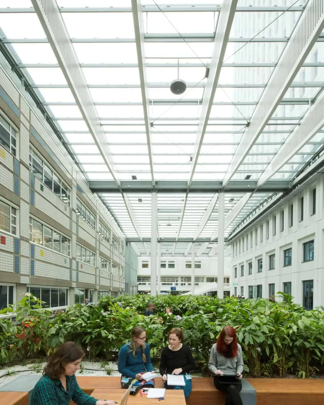 Wit gebouw van binnen met glazen dak, groene planten en mensen