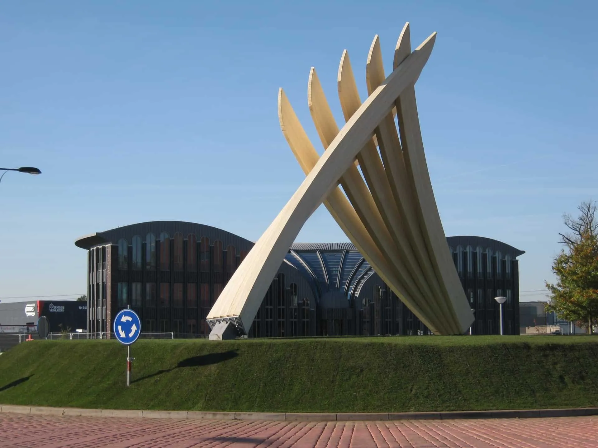 Kunstwerk van houten balken in elkaar verweven op een rotonde met gras erop