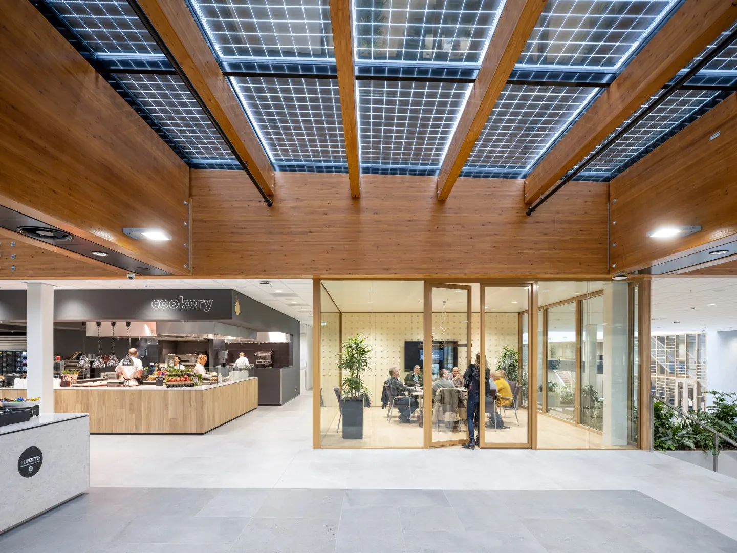 De kantine met houten en glazen plafond met een keuken en glazen ruimte met een tafel en mensen erin