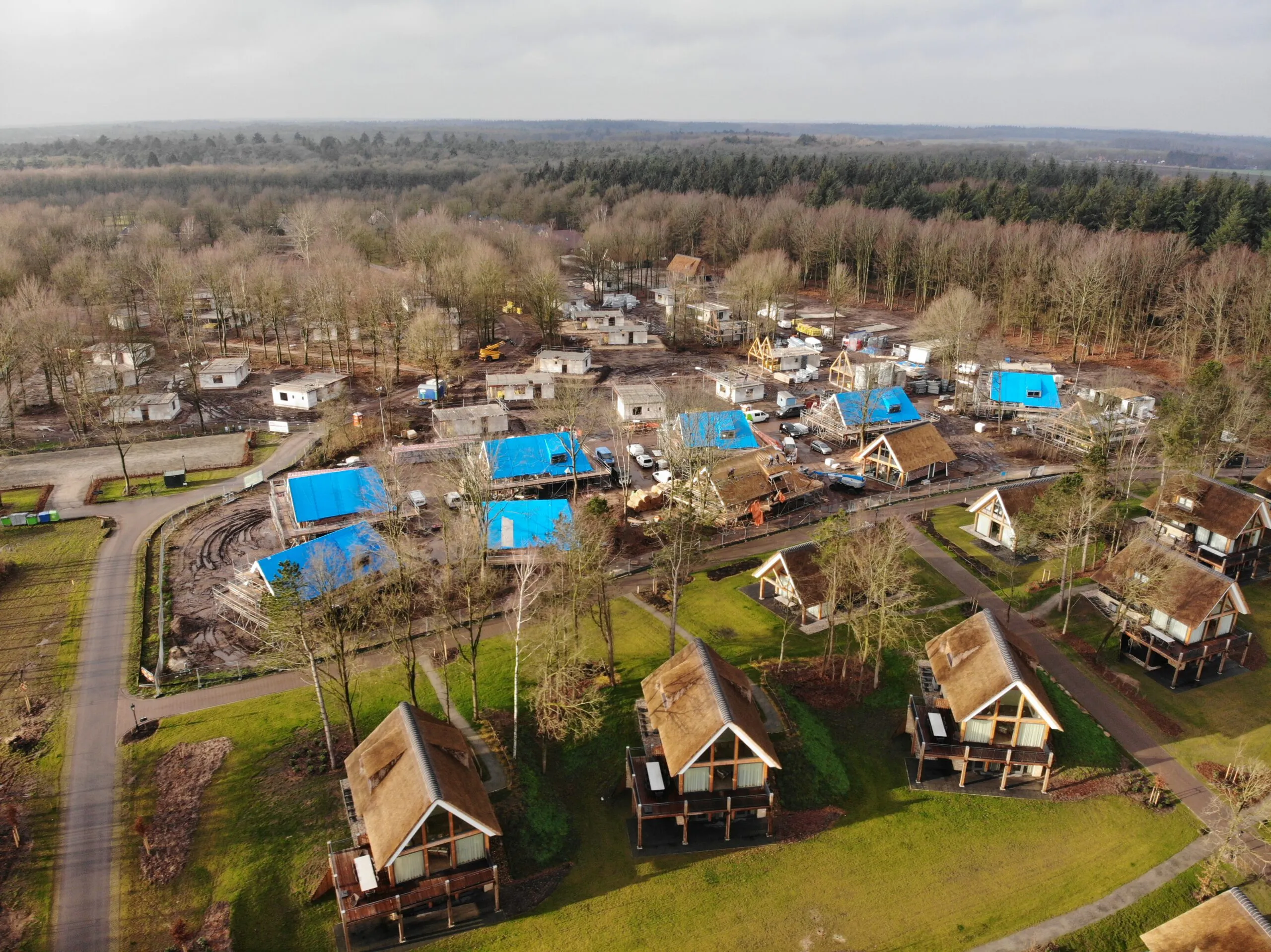 Een vakantiepark van bovenaf met rieten daken en daken in aanbouw in de natuur