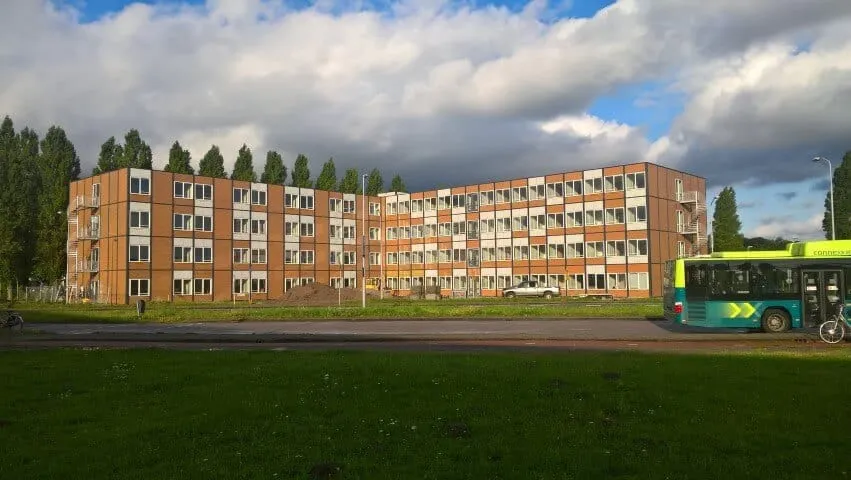 Voorkant houten met wit gebouw aan een weg met grasveld ervoor en een bus