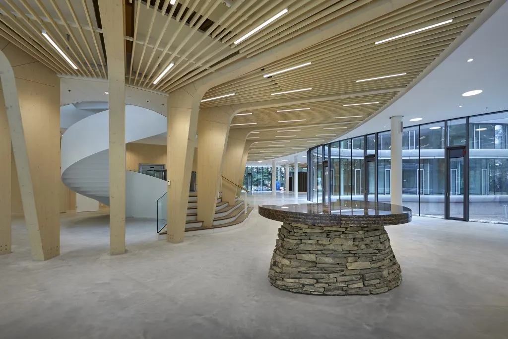 Gelijmde houtconstructies in het interieur van de Triodos bank in Driebergen met stenen tafel in het midden.