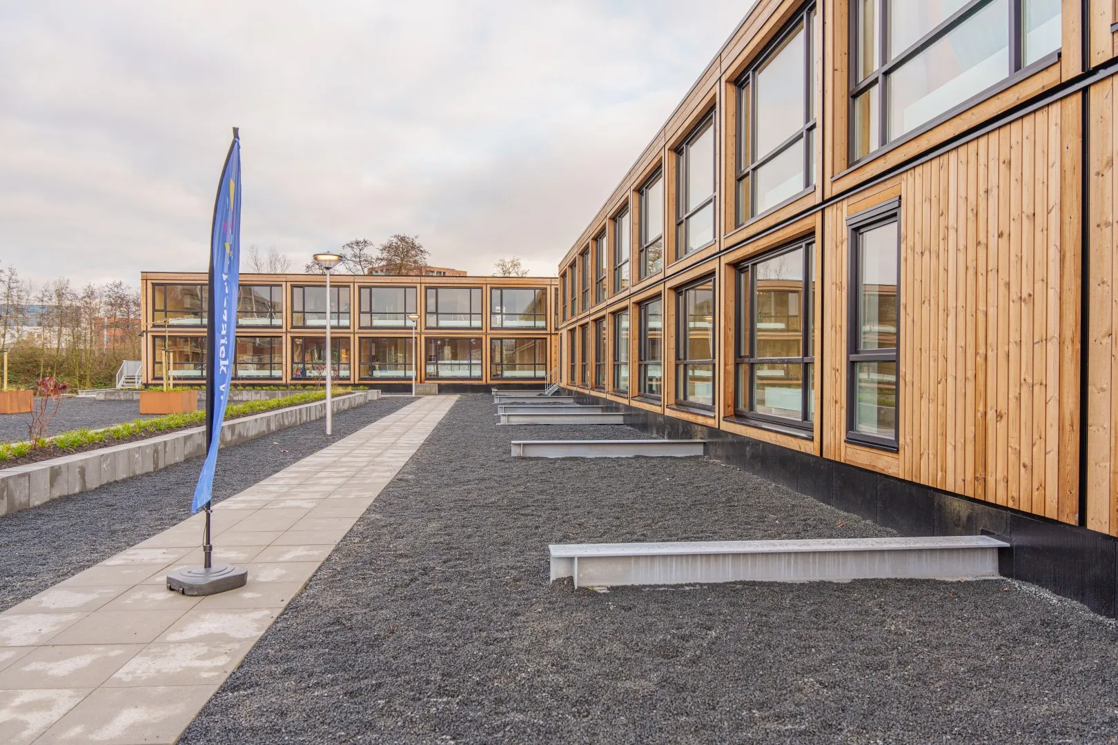 Houten woongebouwen met een pad met een vlag erop en en groenstrook en zandstrook
