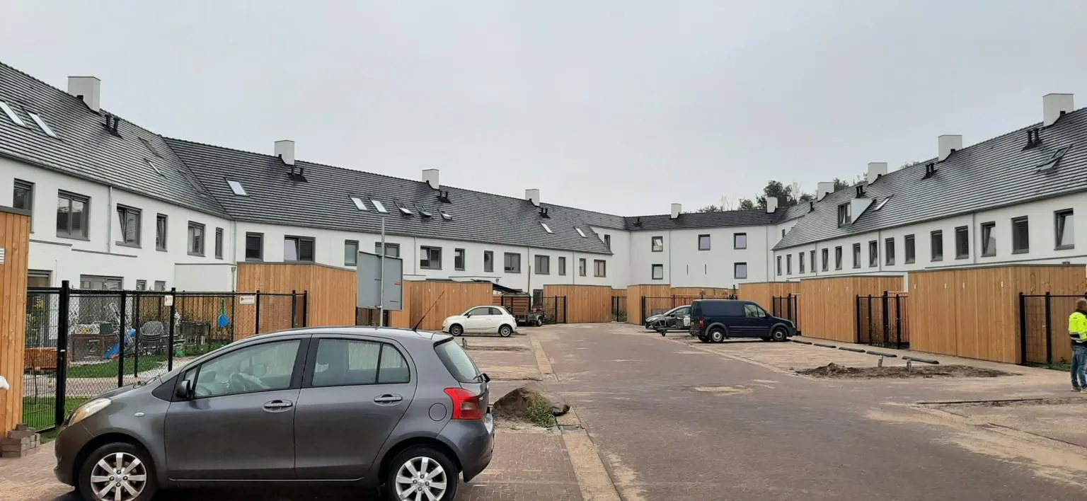 Witte rijtjeshuizen in een woonwijk met houten schuurtjes grenzend aan een parkeerplaats