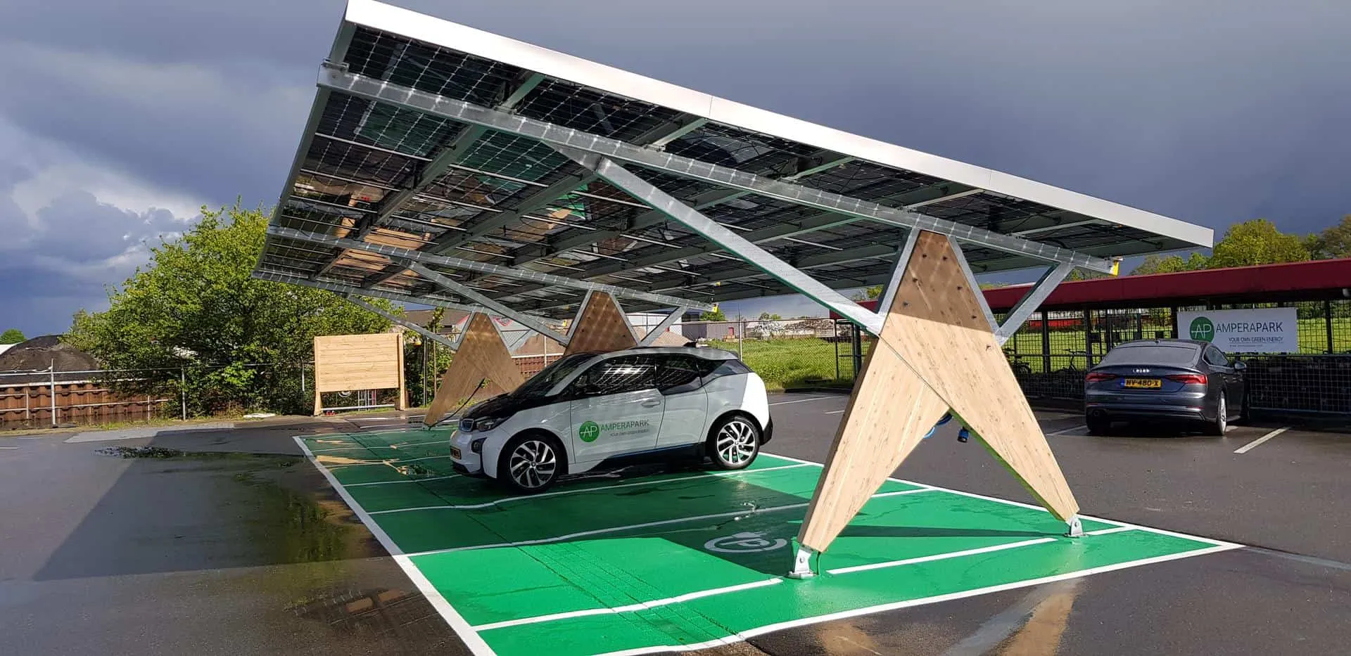 Houten constructie van overkapping met zonnepanelen met een vak van groen asfalt en witte auto