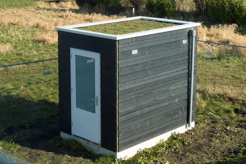Zwart houten schuurtje in een grasveld met gras op het dak