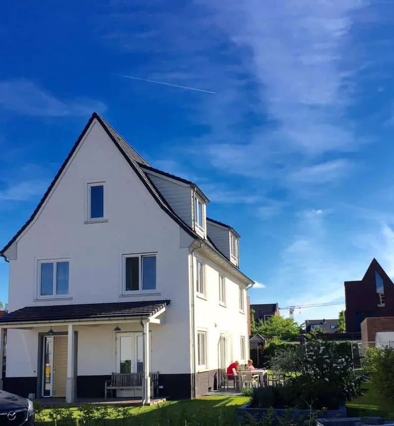 Wit huis met zwart dak en een strak blauwe lucht met sluierbewolking als achtergrond