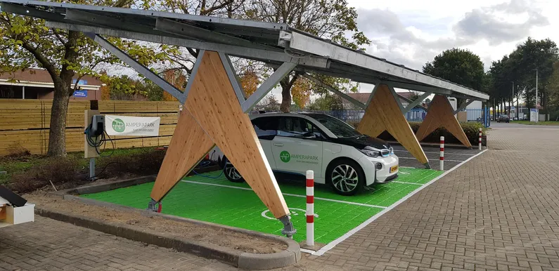 Parkeerplaatsoverkapping van hout met zonnepanelen, groene stenen en wit met rood paaltje