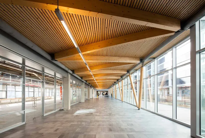 Gang van glazen gebouw van binnen met houten plafond en balken voor de ramen