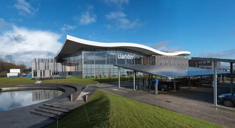 Glazen gebouw met golvend dak met vijver naast grasveldje